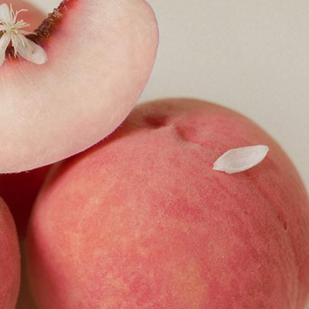 A close-up of soft pink peaches, including one freshly sliced peach with a delicate white blossom resting on it, creating a gentle and natural aesthetic.